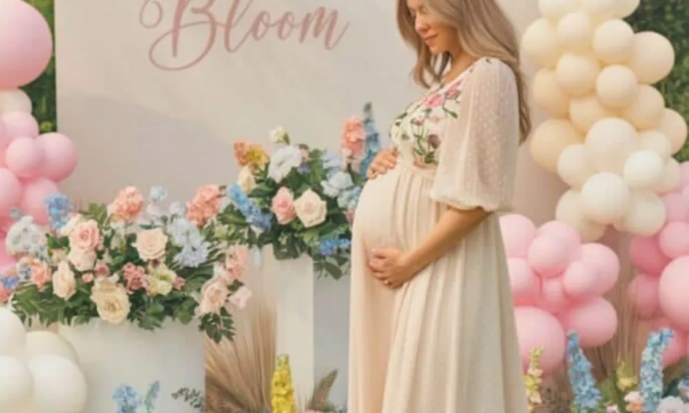 baby shower trivia questions featured in a photo of an expectant mother posing in a floral gown in front of a "Baby in Bloom" backdrop decorated with balloons and flowers.