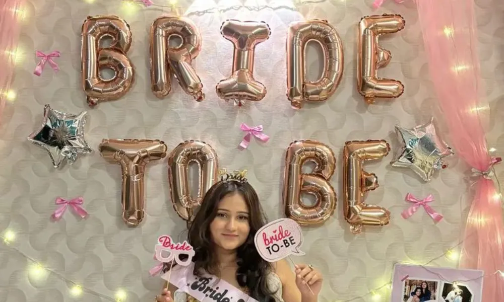 bridal shower trivia questions featured in a photo of a smiling bride-to-be wearing a sash and holding photo props in front of rose gold "Bride To Be" foil balloons.