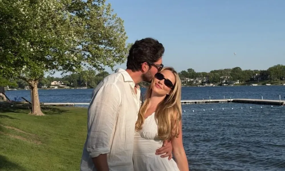 couples trivia questions featured in a photo of a man kissing a blonde woman on the cheek near a waterfront on a clear day.