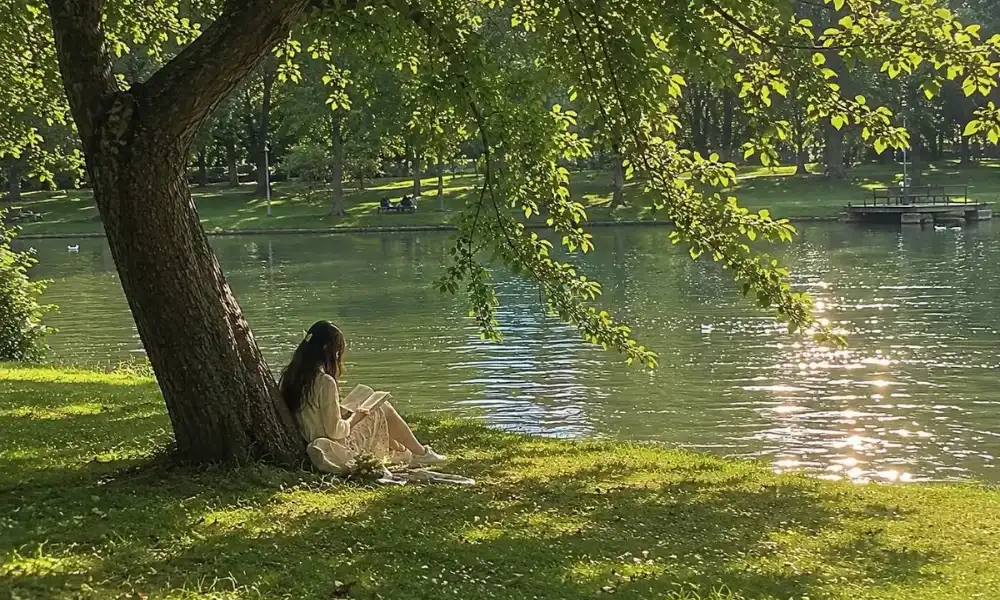 Peaceful nature scene of a girl reading by a lake